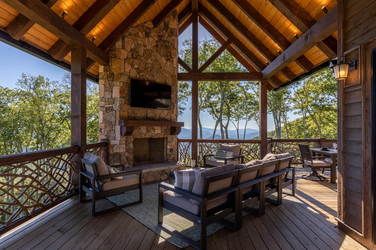 A cozy outdoor living area featuring a stone fireplace, comfortable seating, and wooden beams, all framing a stunning view of the mountains. The setting invites guests to gather around the fire, socialize, and enjoy nature, day or night, blending comfort with the outdoors.