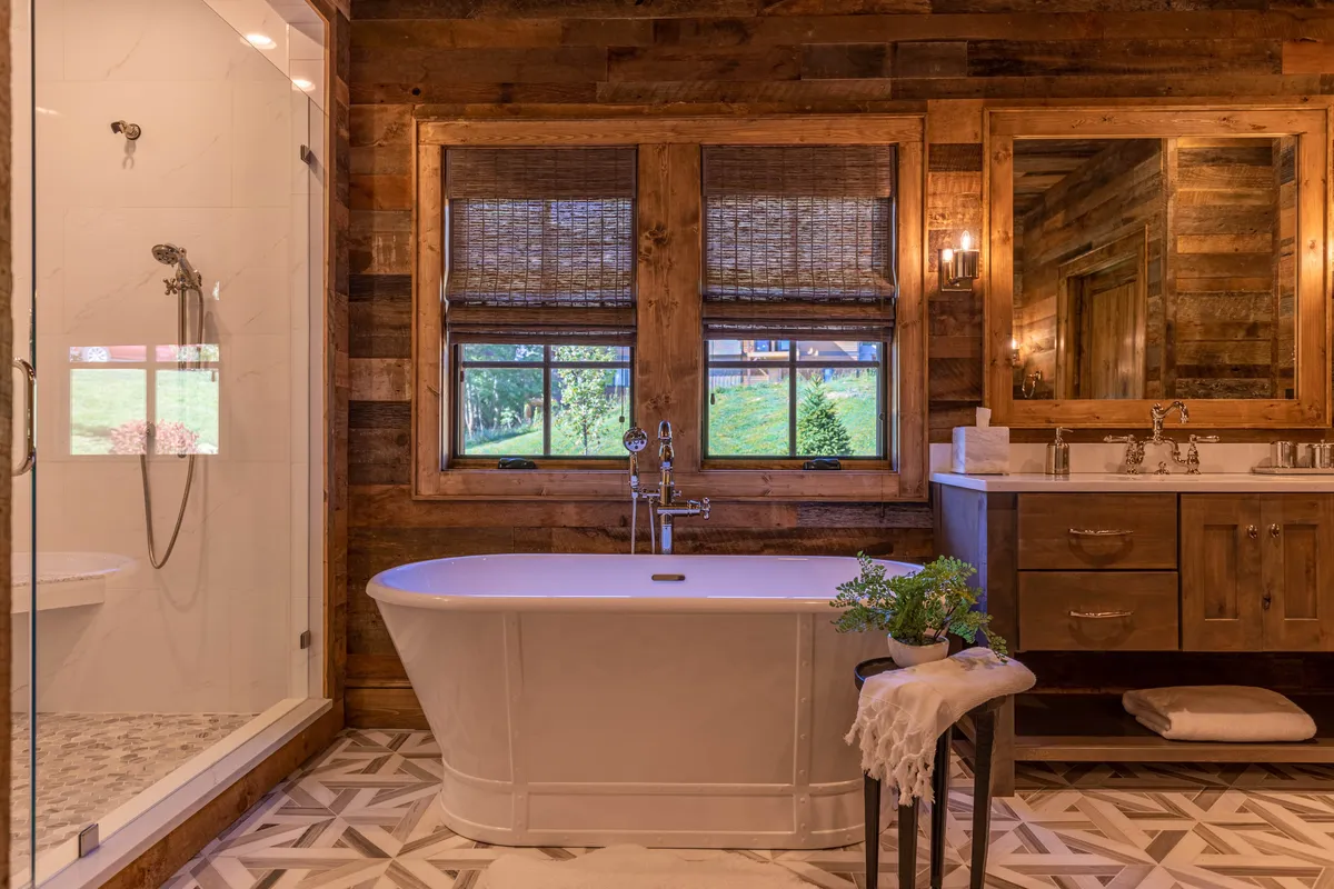 A serene, spa-like bathroom featuring a freestanding bathtub positioned near expansive windows that bring in natural light and highlight the wooden walls. The vanity area and mirror add functionality while maintaining the restorative, peaceful vibe.