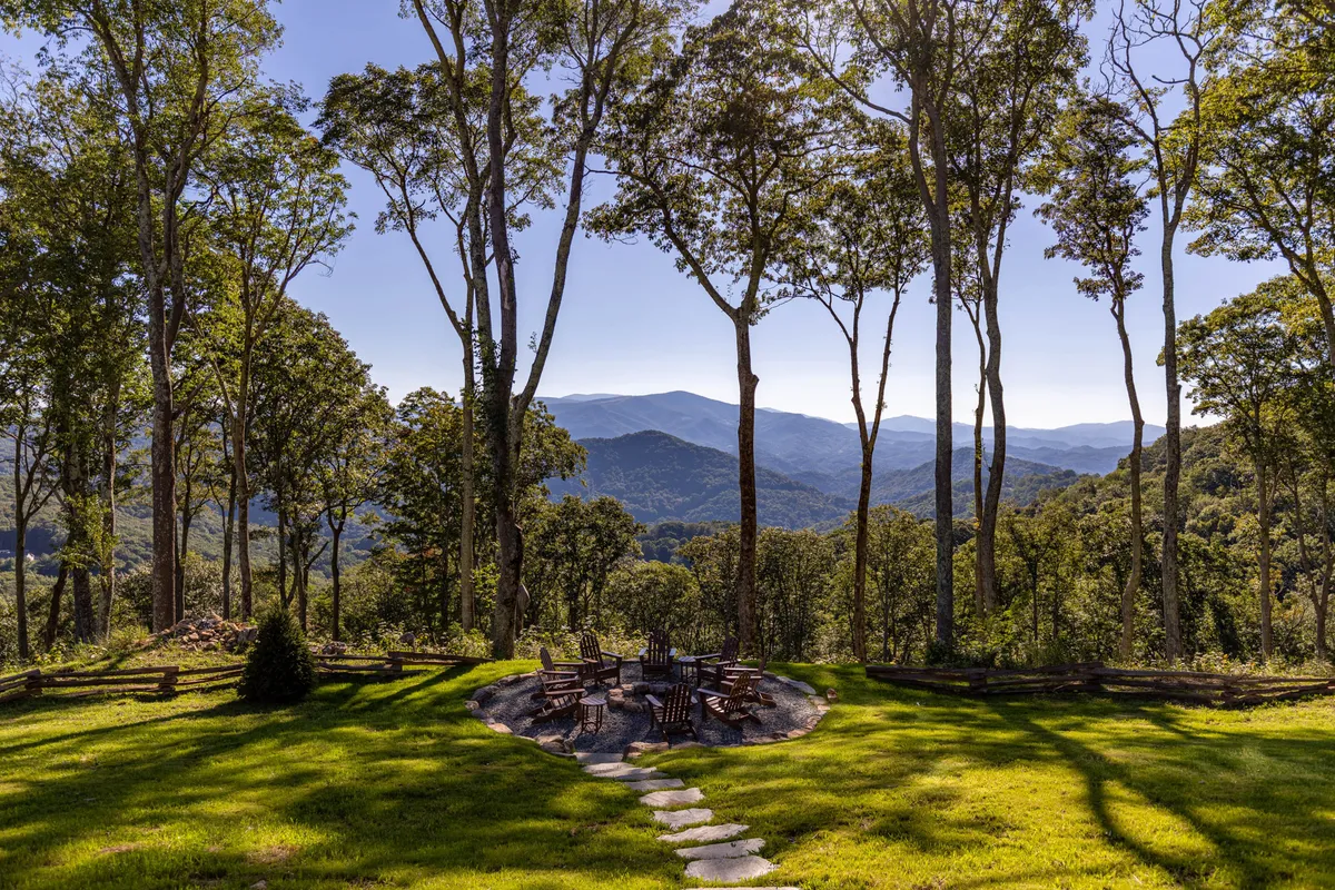 An inviting fire pit scene with Adirondack chairs arranged around the flames, offering panoramic mountain views and tall trees in the background. The space is designed for relaxation, storytelling, and creating warm memories under the open sky.