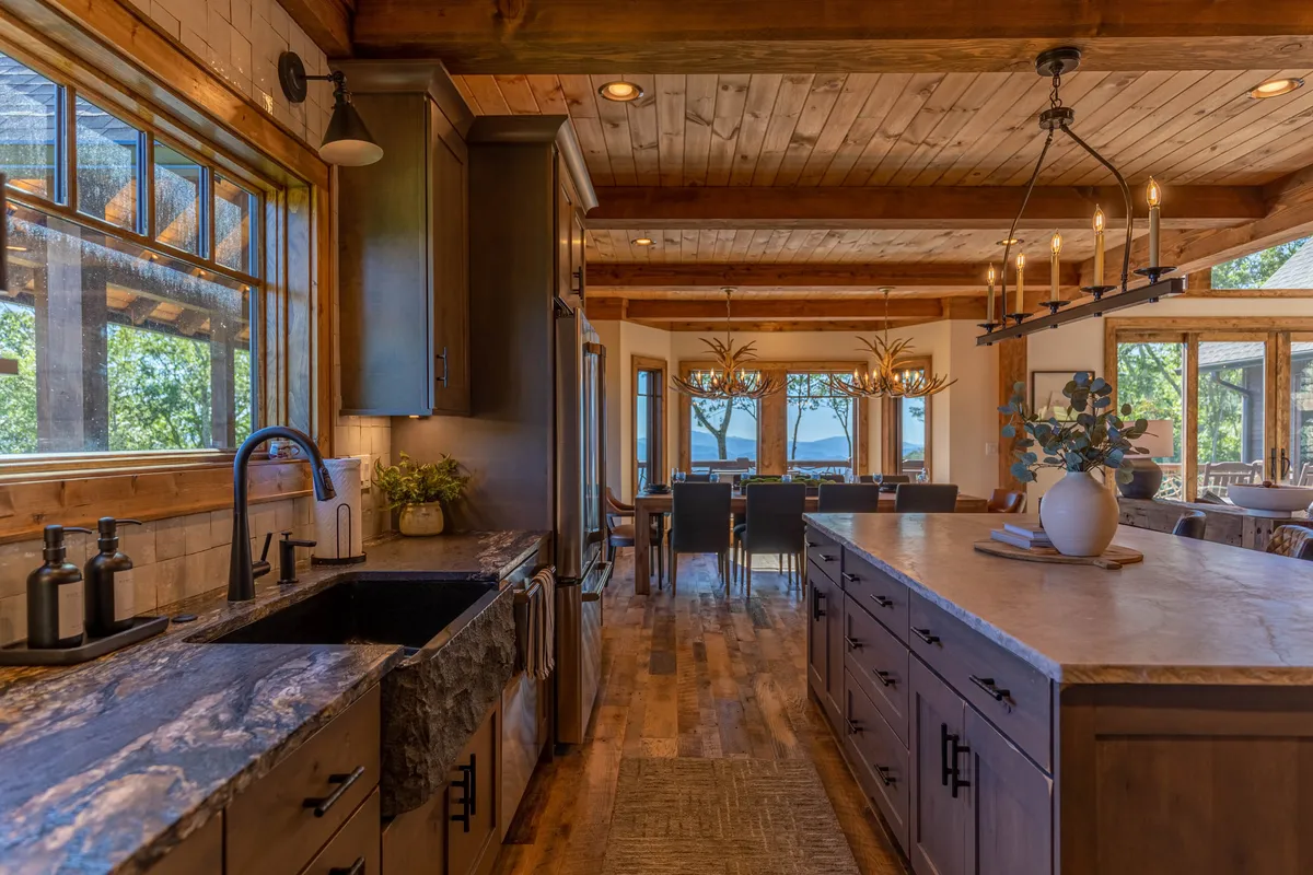 A seamless open-plan kitchen and dining area with a spacious island, stylish chandelier, large windows, and an inviting dining table—all flowing naturally into the living space.