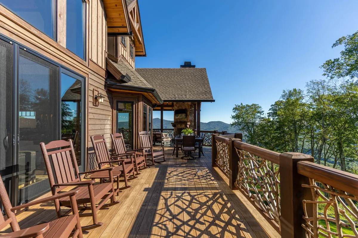 A covered deck with wooden railings, rocking chairs, an outdoor dining set, and a cozy fireplace—all oriented toward sweeping mountain views. The space is designed for relaxation and socializing, offering an ideal vantage point to enjoy sunrises, sunsets, or post-activity gatherings.