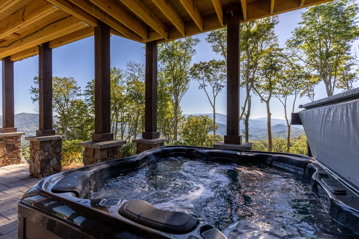 A serene outdoor hot tub surrounded by wooden beams and trees, with sweeping mountain views in the background. The setting exudes tranquility and invites relaxation while connecting guests to the beauty of the outdoors.