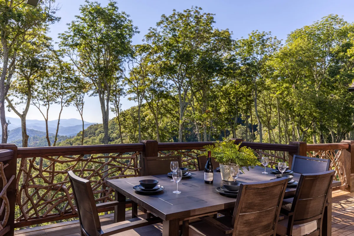 An elegant outdoor dining area with a table set for a meal, framed by decorative railing and panoramic mountain views. The setting is ideal for wine tasting, sunset dinners, or morning coffee with friends, emphasizing the connection between upscale leisure and the natural beauty surrounding Eagles Nest.