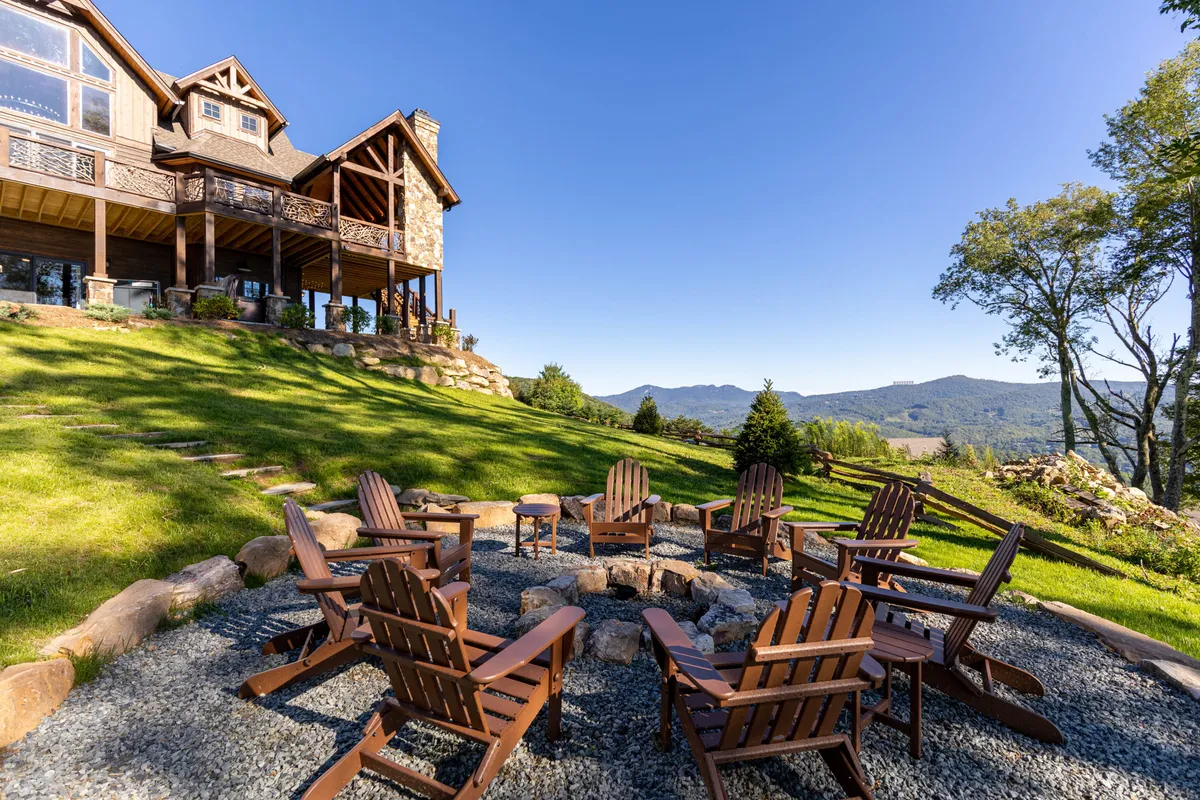 A cozy fire pit setup with Adirondack chairs sits on a landscaped lawn facing a mountain view. The scene suggests a relaxed, communal atmosphere perfect for families to gather around the fire, enjoying sunset views and evenings outdoors.